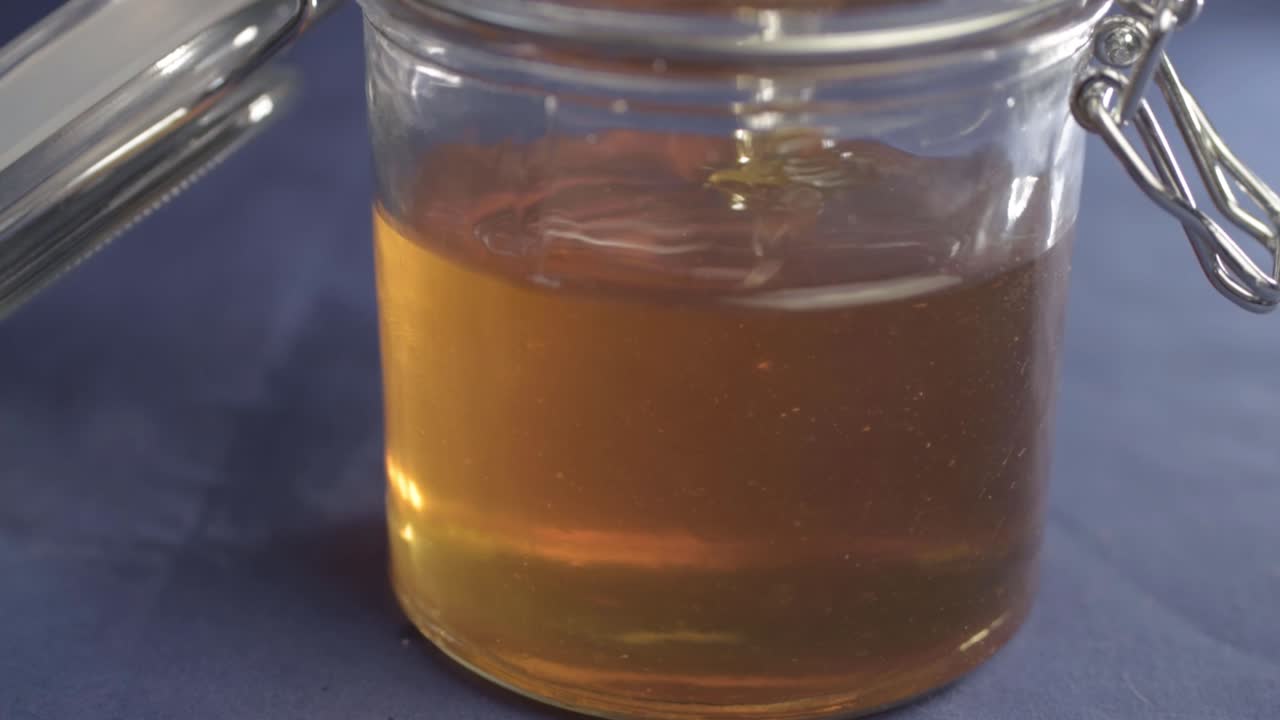 Pouring golden runny honey into a glass jar close up