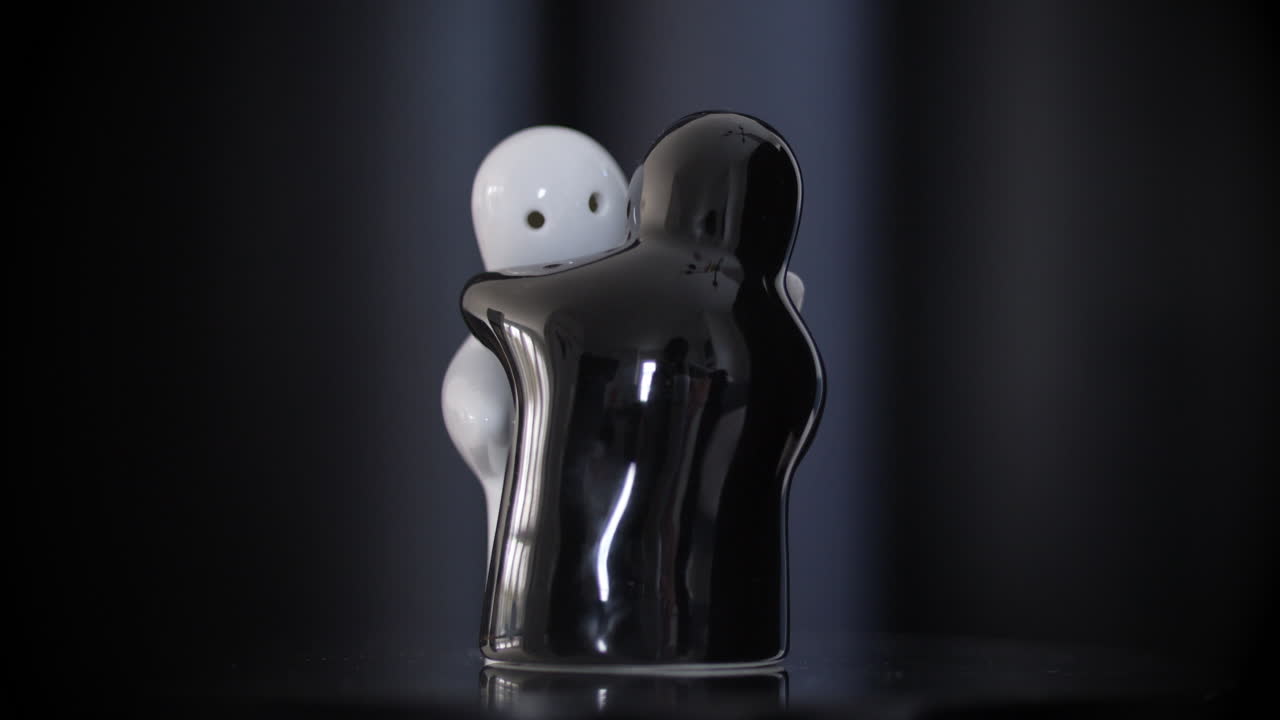 estatuetas de porcelana abraçando preto e branco girando na superfície reflexiva, fundo preto
