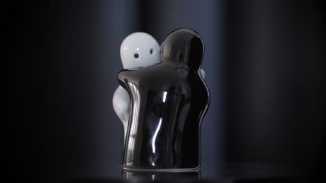 black and white hugging porcelain figurines rotating on reflective surface, black background