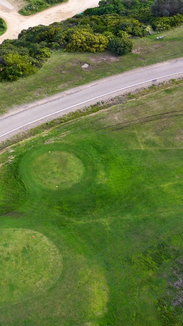 High-angle drone shot panning over lush golf greens and coastal vegetation in Flinders, Australia.