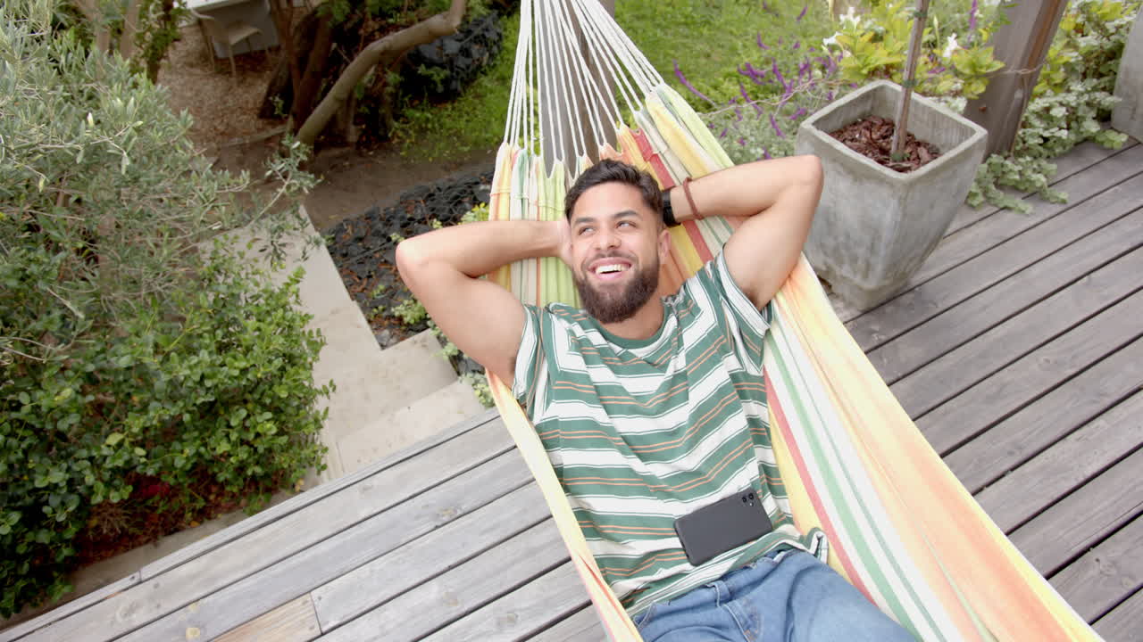 Relaxing in hammock, man smiling and enjoying leisure time outdoors