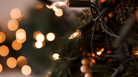 Rack-Fokus-Nahaufnahme-Von-Glitzernden-Kugeln,-Die-An-Einem-Weihnachtsbaum-Mit-Lichterketten-Und-Bokeh-Hängen