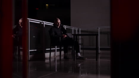 man sitting on balcony at night looking at phone