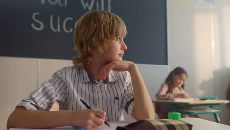 niño pensativo sentado en el escritorio en el salón de clases. escolar mirando por la ventana