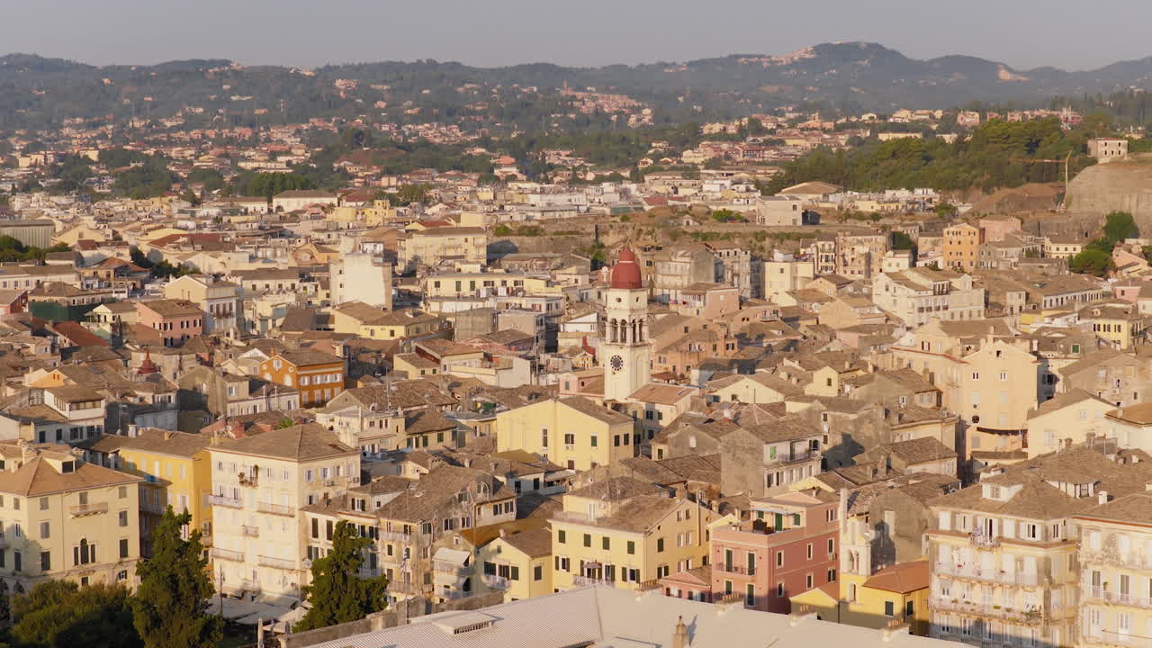 Saint Spyridon Church at sunrise with birds flying over rooftops in Corfu Old Town, wide overview drone aerial descend