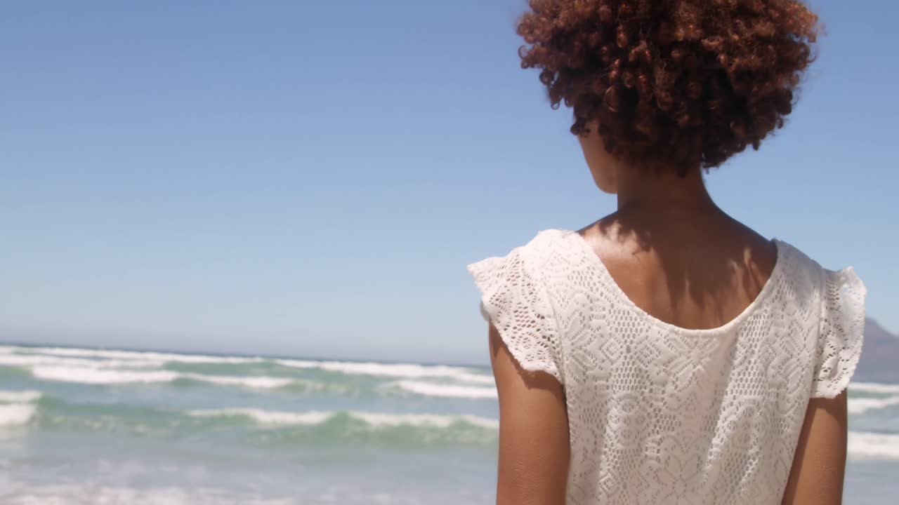 Rear view of young African american woman walking on beach in the sunshine 4k