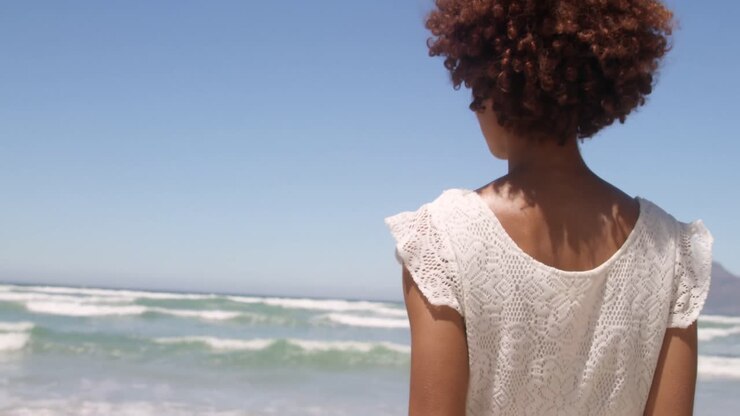 Rear view of young African american woman walking on beach in the sunshine 4k