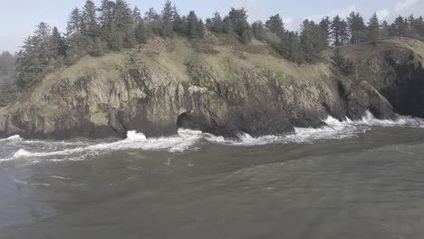 Brown-water-ocean-waves-crash-up-against-the-rough-rugged-Washington-coastline,-aerial-track