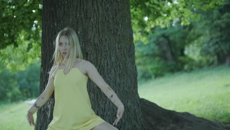 mujer con vestido amarillo bailando junto al árbol en el parque de verano