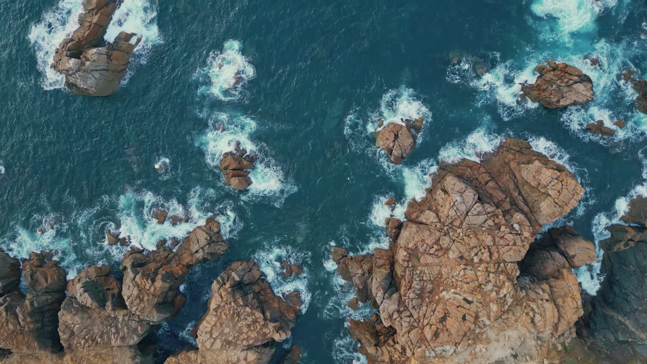 Onde azzurre che schiumano sulle rocce, vista dall'alto. Oceano blu rilassante che lambisce le scogliere.