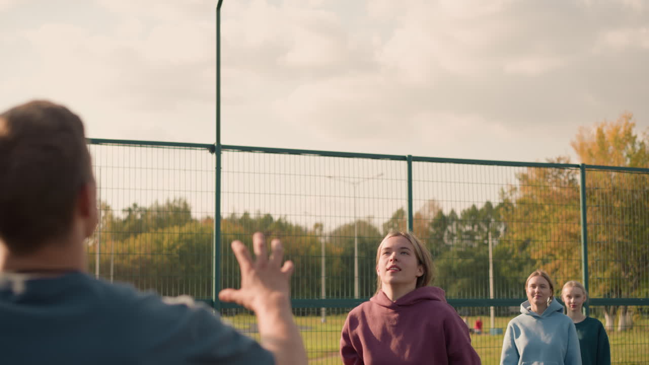 두 명의 팀 동료가 지켜보는 가운데, 배경에서 볼 수 있는 축구장, 은 하늘과 야외 스포츠 코트