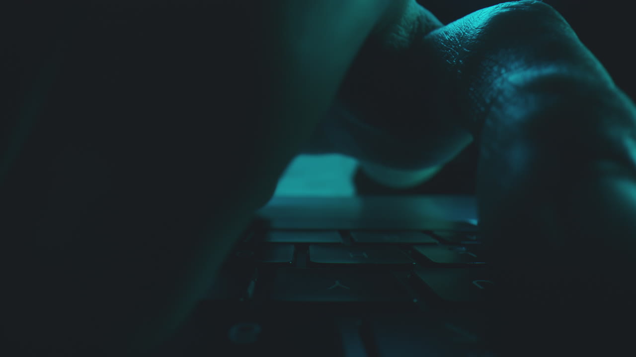 Close up of hands typing on a laptop keyboard at night.