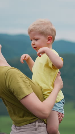 little son takes mother hair away and puts head onto shoulder against valley and misty mountain range at resort on rainy day slow motion