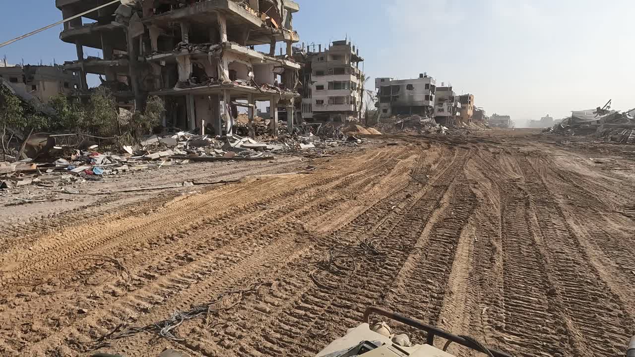 Striscia di Gaza — Riprese POV da un veicolo militare che si muove attraverso un'area urbana gravemente danneggiata con edifici distrutti e detriti lungo una strada sterrata.