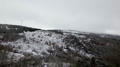 Toma-Aérea-De-Una-Colina-Nevada-Con-Vegetación-Invernal-Y-Horizonte-Nublado-Y-Brumoso