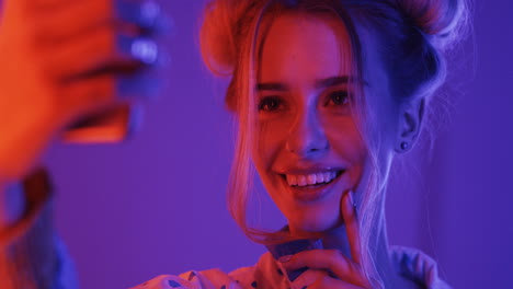 close up of blonde young girl taking selfie photo on the smartphone on the pink and violet neon light background