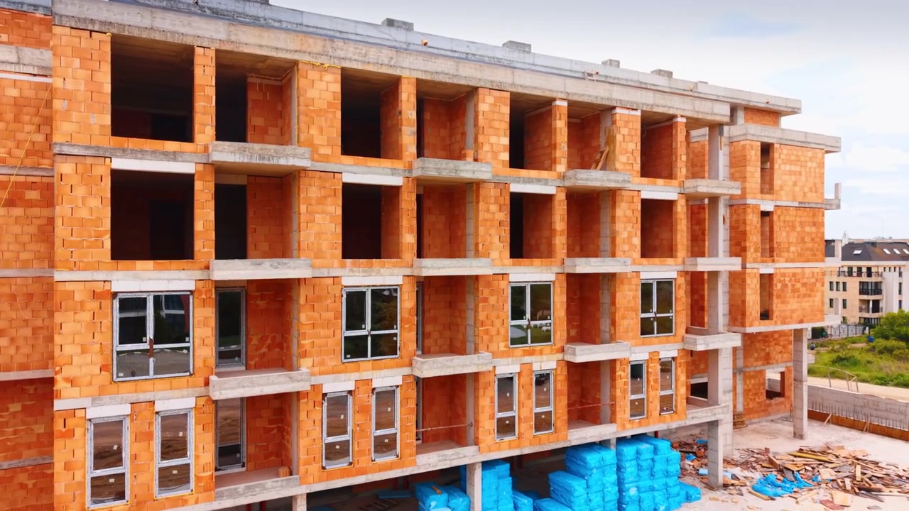 Betonová a cihlová konstrukce projektu nového obytného domu. Detailní pohled na betonové sloupy a červené cihlové zdi rozestavěné budovy.