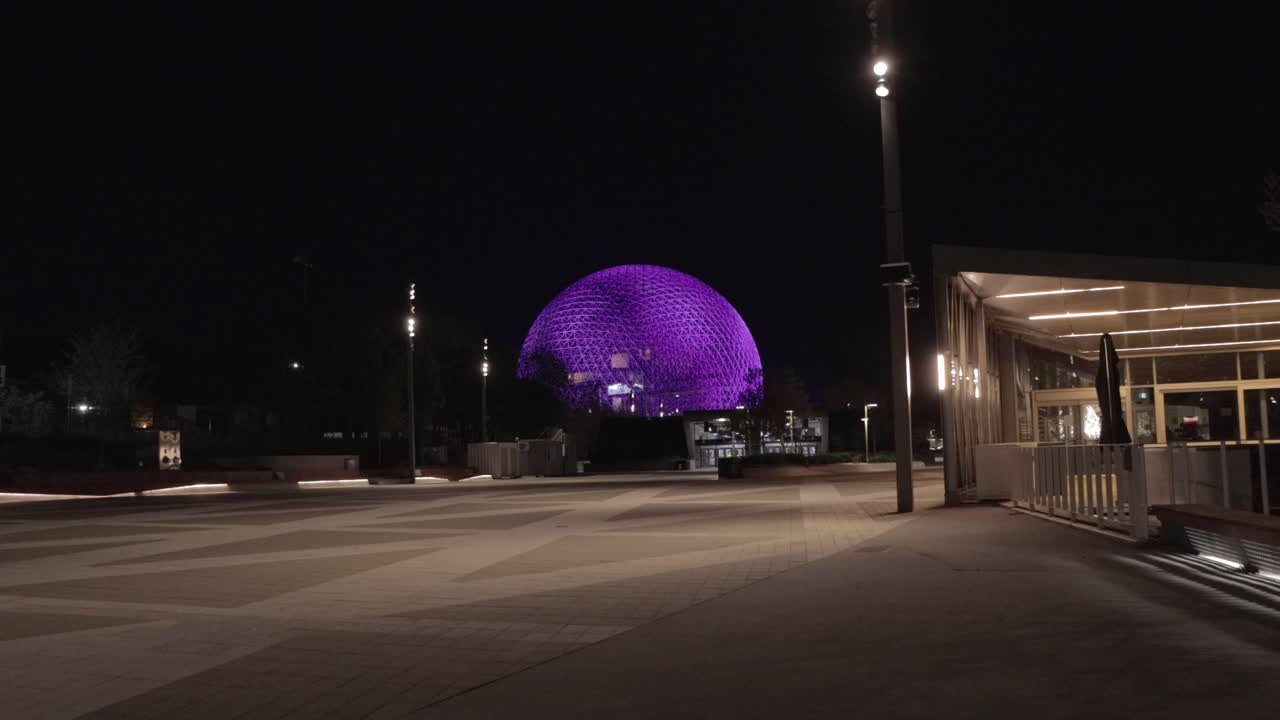 una foto amplia del parque jean drapeau con la biosfera iluminada de púrpura por la noche en montreal, quebec