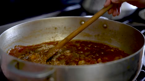 wooden spatula stirring simmering curry sauce with spices in large pot