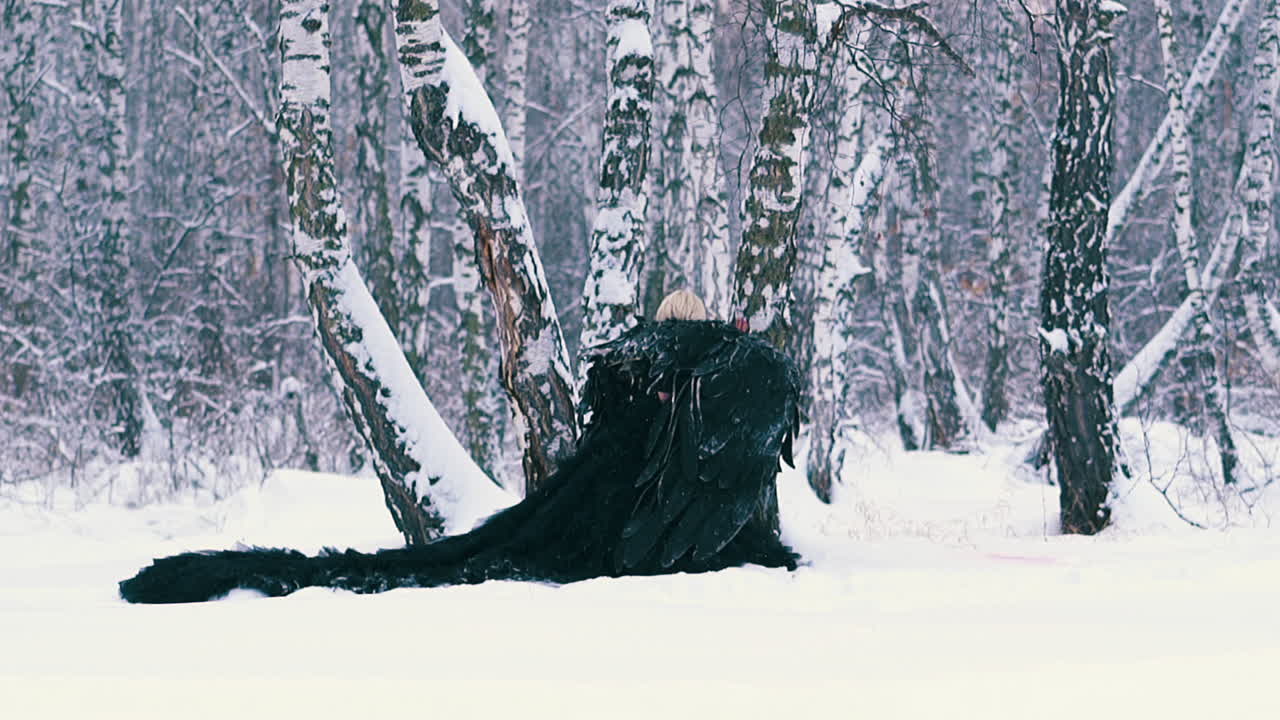 날개를 단 피닉스 양복을 입은 여자가 숲속의 나무에 쪼그리고 앉는다