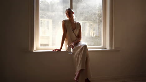 woman sits thoughtfully on a windowsill bathed in natural light