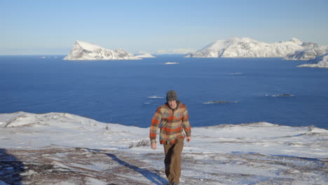 a man hiking up a snowy landscape with the arctic ocean and mountains in the background