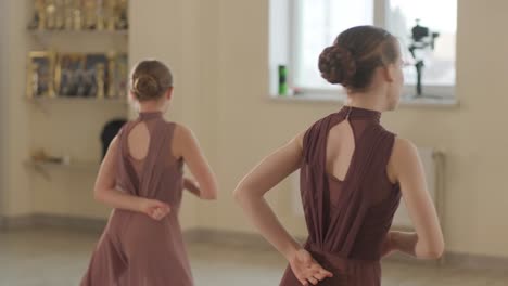 a group of young ballet students in black dancewear practicing positions in a spacious ballet studio with wooden flooring and wall-mounted barres. focused expressions and synchronized movements.