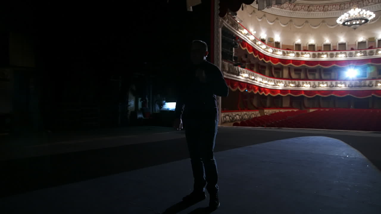 Theater actor has rehearsal before performance. Dark light behind scene. Man in formal clothes with handfree microphone. Classic theater concept.