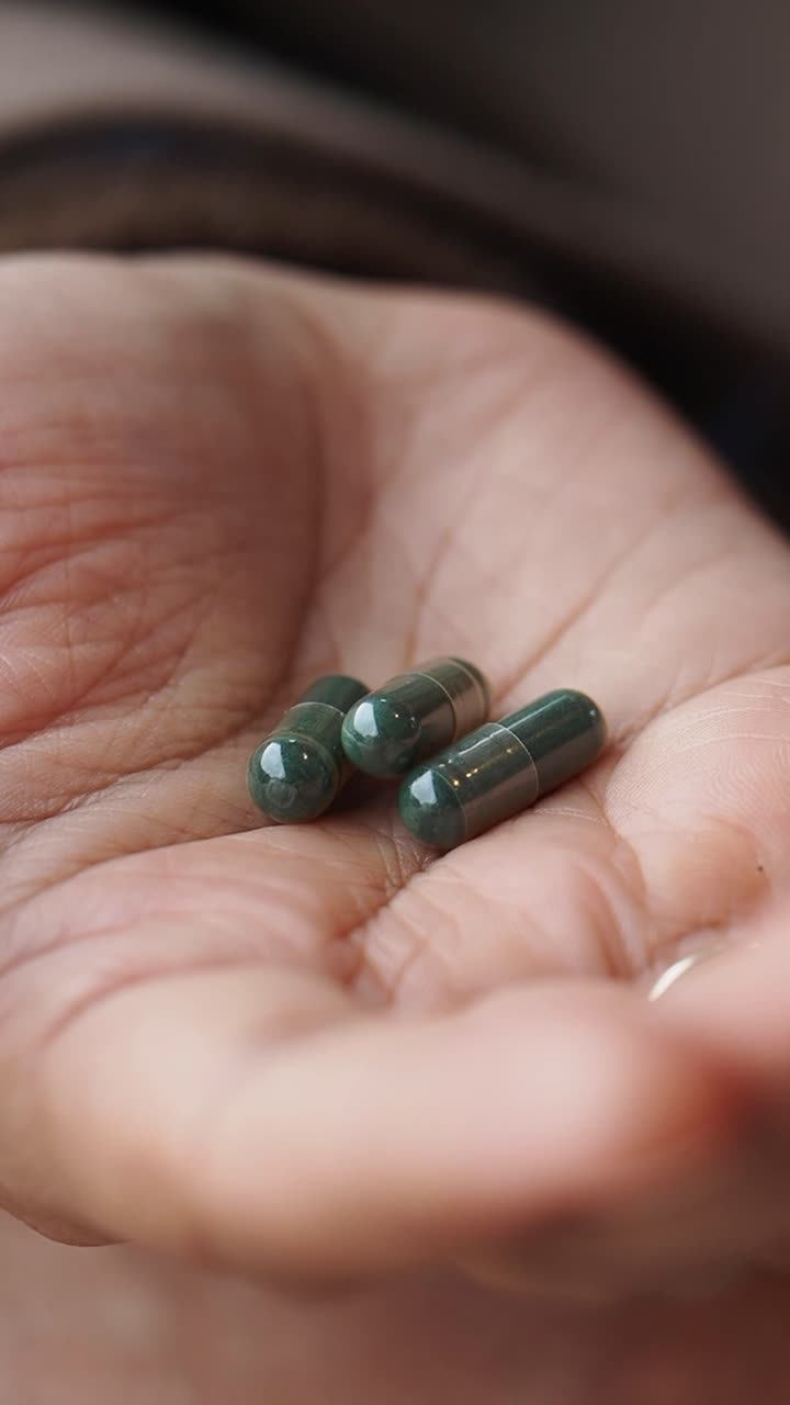 Primo piano di una mano che tiene e prende capsule verdi.