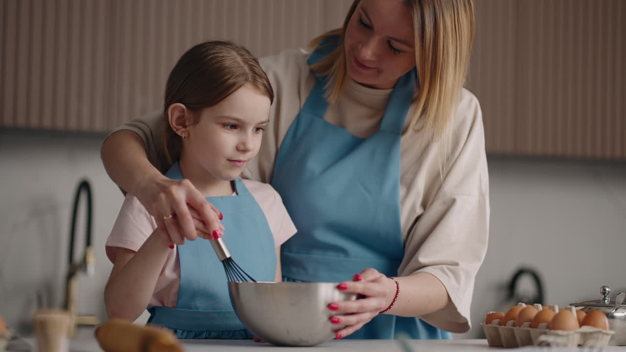 una niña en edad preescolar y su madre están cocinando en la cocina de la casa. la madre está enseñando a la hija a cocinar.