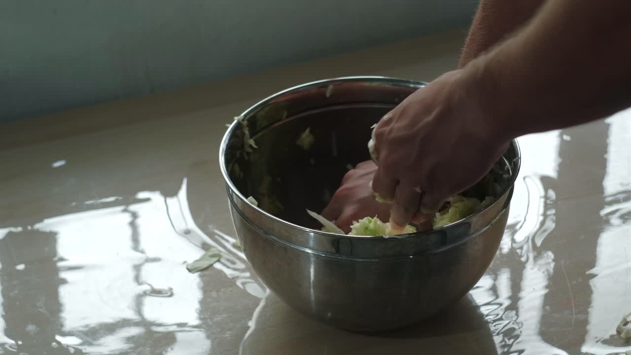 Overhead medium shot of hands massaging sliced cabbage in a bowl for sauerkraut preparation.