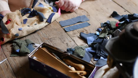 close-up of hand working with textile pieces on a wooden table, alongside sewing tools