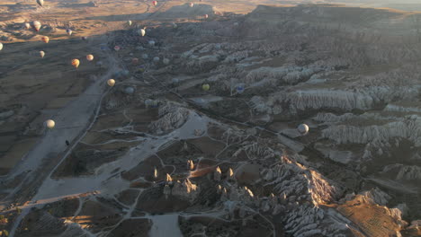 Vista-Aérea-Del-Paisaje-De-Cuento-De-Hadas-De-Capadocia,-Turquía-Con-Globos-Aerostáticos-Volando-Por-Encima-En-La-Mañana-Soleada,-Disparo-De-Drones