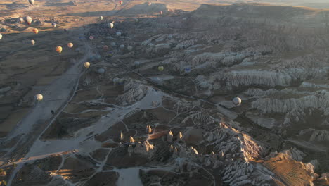 aerial view of fairytale landscape of cappadocia, turkey with hot air balloons flying above on sunny morning, drone shot