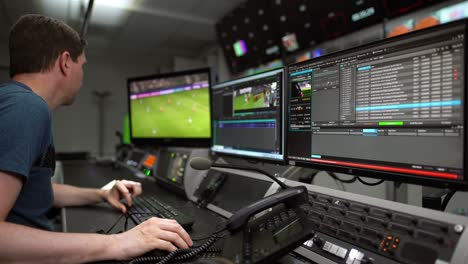 Man-at-work-in-a-TV-company---cutting-a-sport-video-sitting-on-a-table-in-front-of-some-monitors-and-communication-elements-like-a-intercom-and-a-telephone