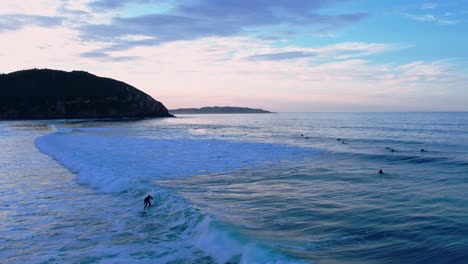 Vista-De-Pájaro-De-Un-Surfista-Montando-La-Ola-En-La-Playa-De-Berria-En-Cantábrico,-España-A-La-Hora-Azul