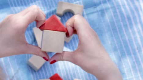 defocused blurred 4k video.house from wooden cubes in woman's hand, red color nail, blue blanket and another eco toys in background. mortgage property insurance, personal own home concept. copy space.