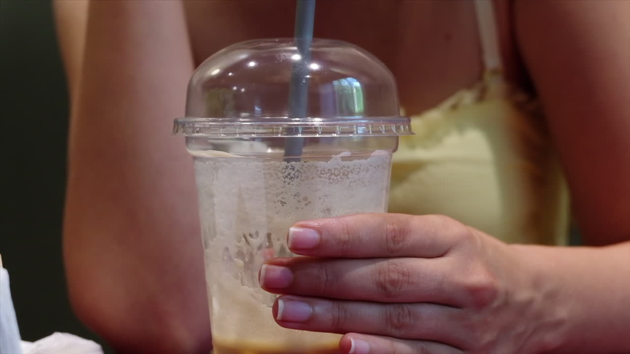 Close up of a woman in a yellow dress drinking an iced latte at a cafe