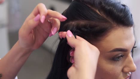 close up of hairdresser plaiting braids to brunette girl in beauty salon. slow motion. close up