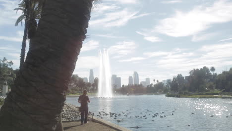 single man goes fishing standing up at echo park lake, with downtown la city in background