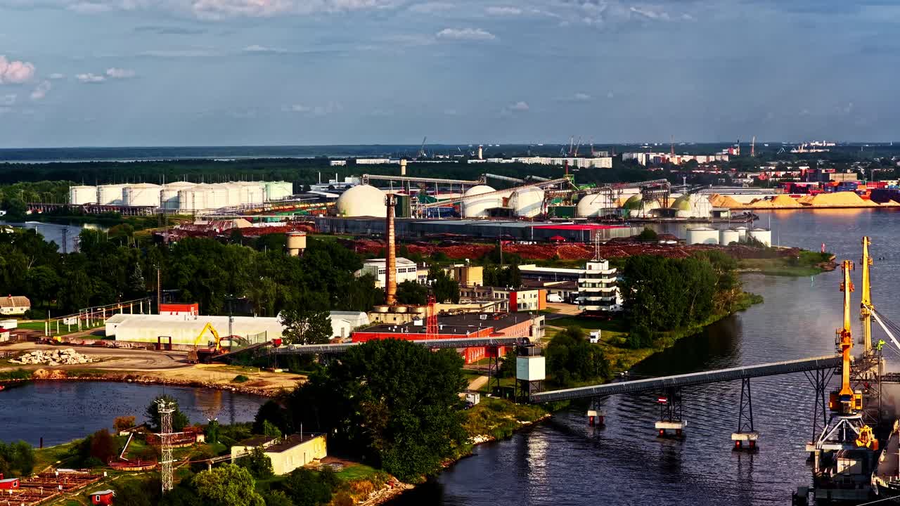 High angle aerial of a sprawling industrial port with oil tanks, colorful shipping containers, cranes, and moored cargo vessels