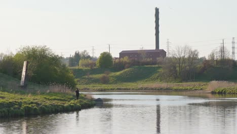 woman fishing by the river near an old electrical substation on a sunny evening