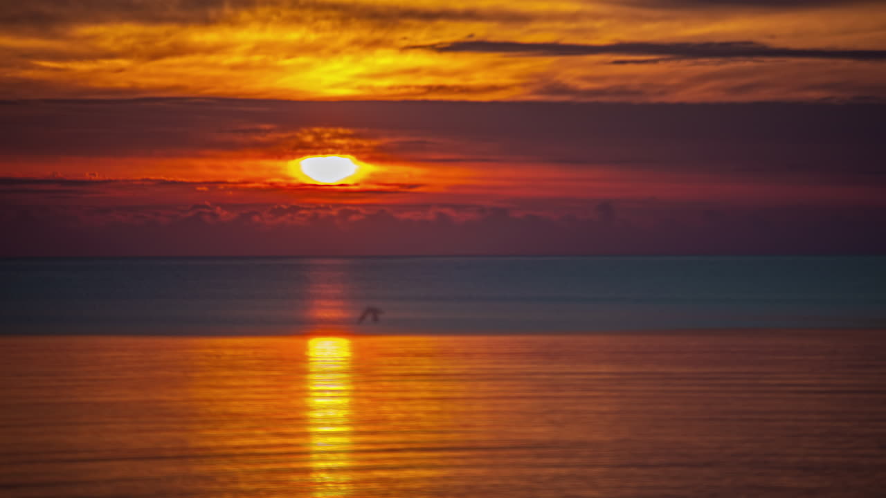 Time Lapse View Of Majestic Golden Setting Sun Behind Clouds On Horizon Over Reflective Seascape