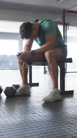 vertical video: resting on bench, man holding water bottle after workout in gym