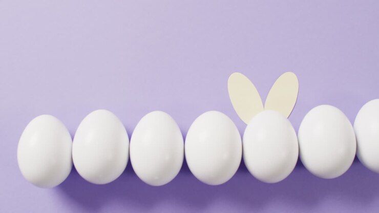 White easter eggs with rabbit ears on purple background with copy space