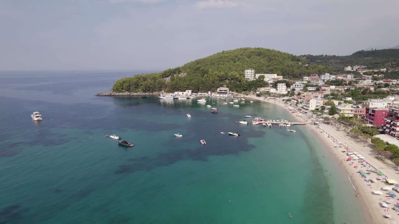 Vista aerea di acque tranquille, barche, spiaggia di sabbia bianca, presso il pittoresco villaggio di Himare sulla costa del Mar Ionio.