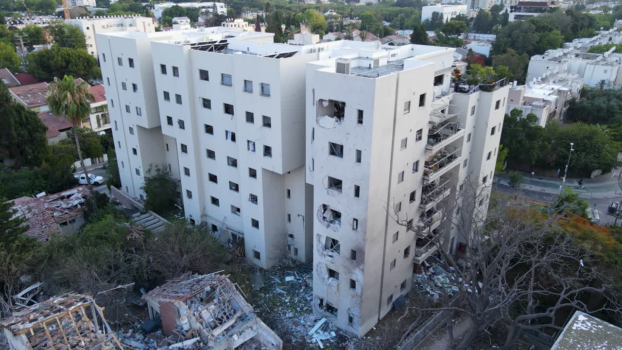 Light drone orbit around a white building in Tel Aviv with shattered windows and visible impact damage.