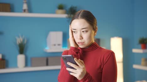 아시아 여성이 스트레스를 받고,  ⁇ 드폰 화면에서 보는 것에 겁을 먹고 있습니다.