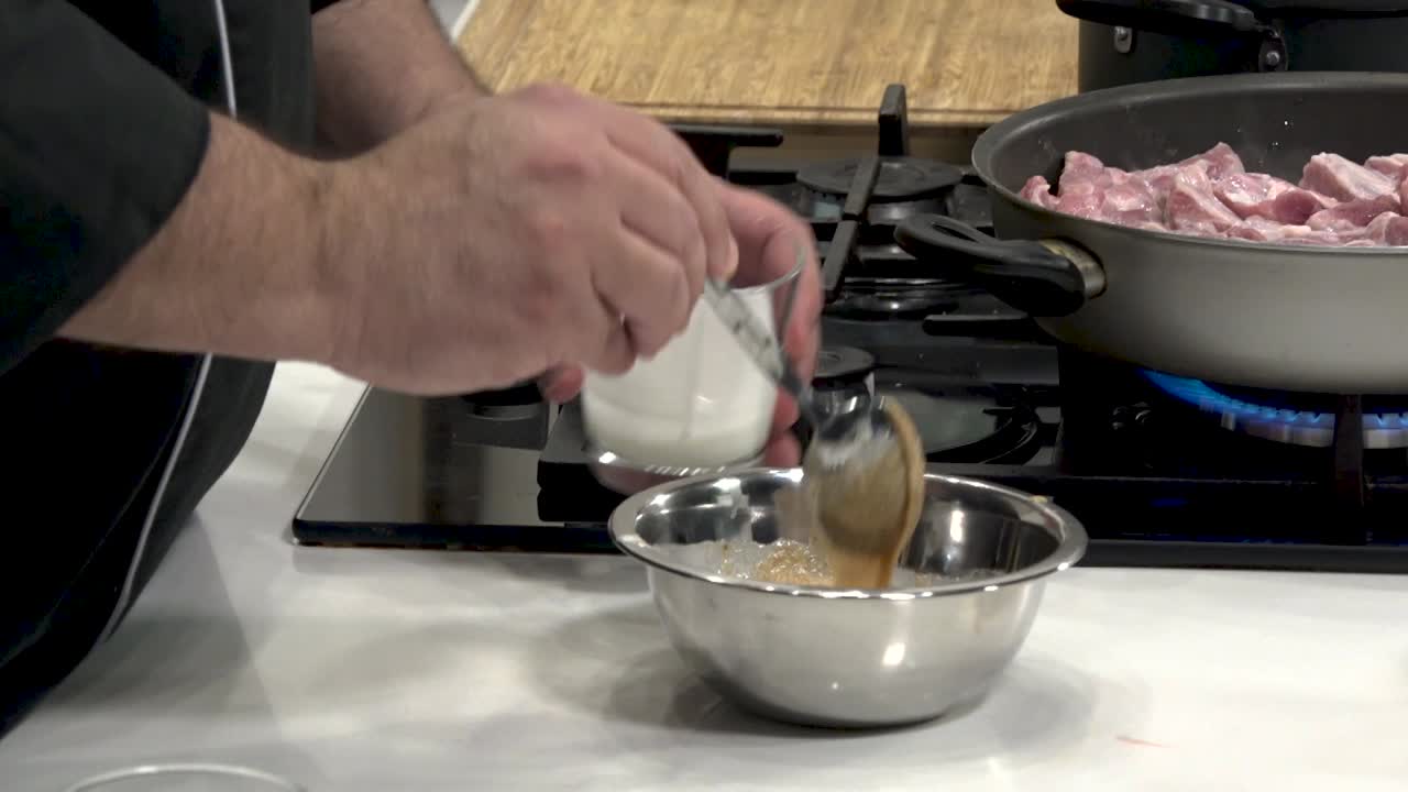 In a contemporary kitchen, a chef prepares a seasoning blend as meat sizzles in a pan. Precision and technique enhance the culinary experience.