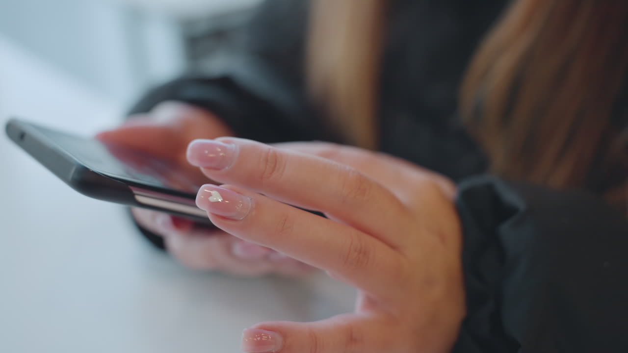 Closeup hands on phone, cafe table commuter taps screen with manicured nails, jacket sleeve visible shallow focus bokeh creates tense atmosphere suggesting potential snatcher and theft risk emphasis
